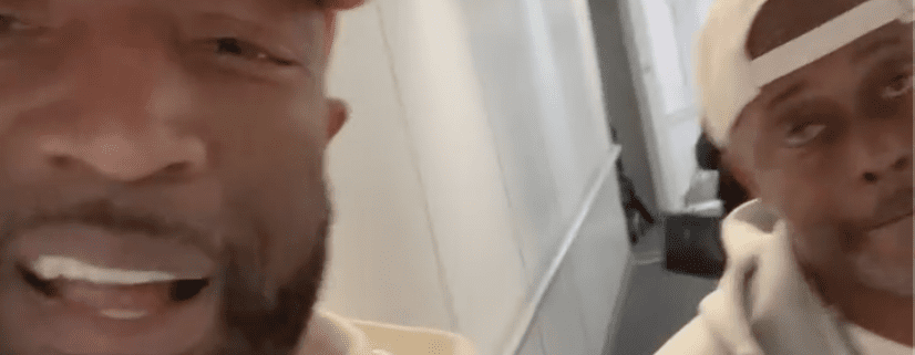 Two men smiling in a hallway.